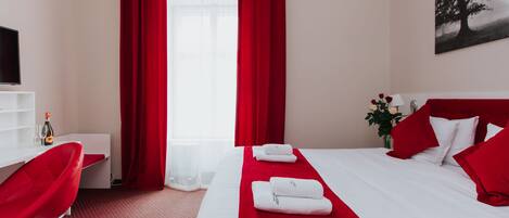 A hotel room with a bed, red curtains, a TV, a desk, and a chair.