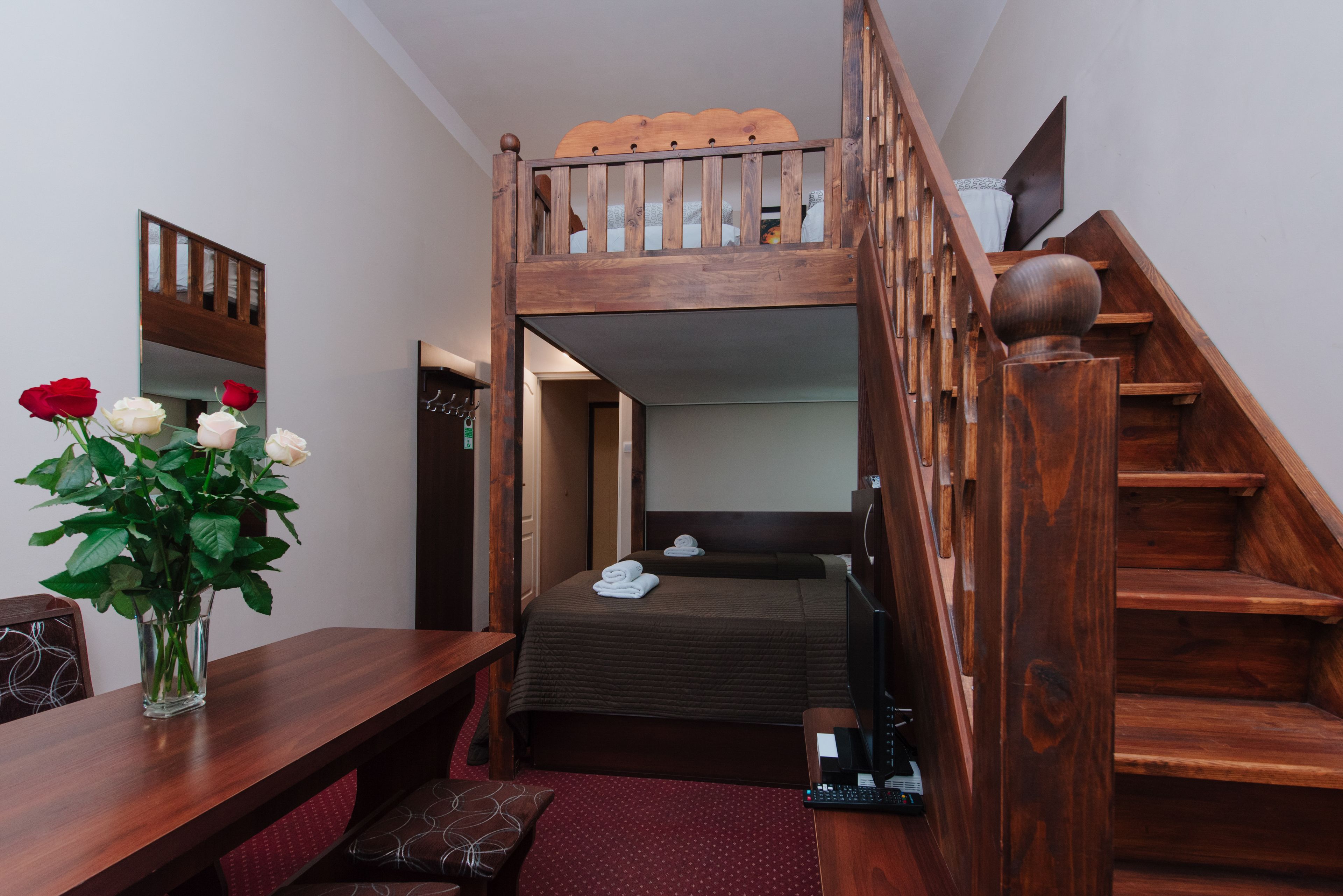 A room with a bunk bed, a wooden desk with a vase of flowers, and a staircase.