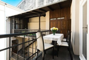 A balcony with a table and chairs, a wooden door, and a view of the building's interior.
