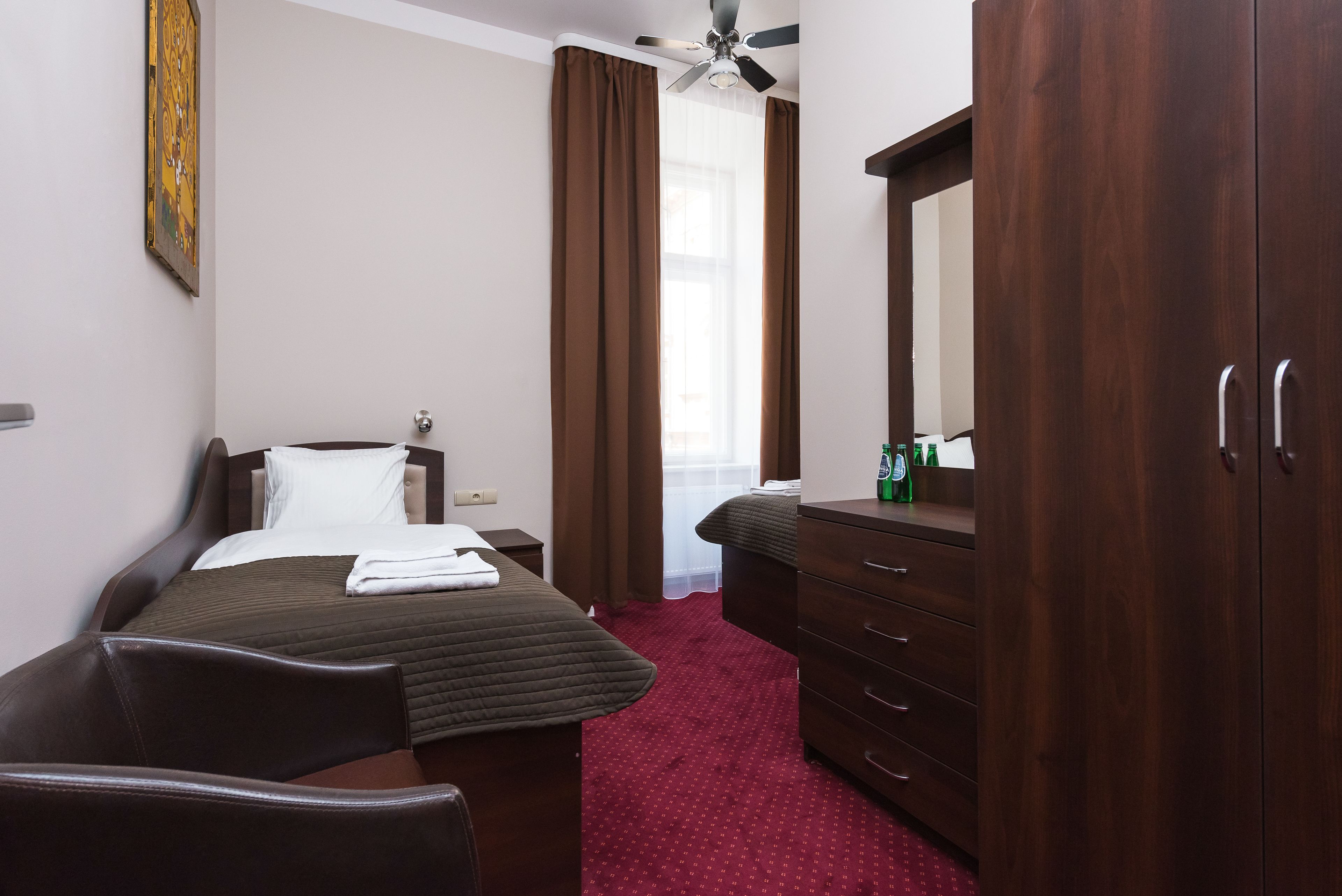 A hotel room with a bed, a dresser, a mirror, a ceiling fan, and a window with curtains.
