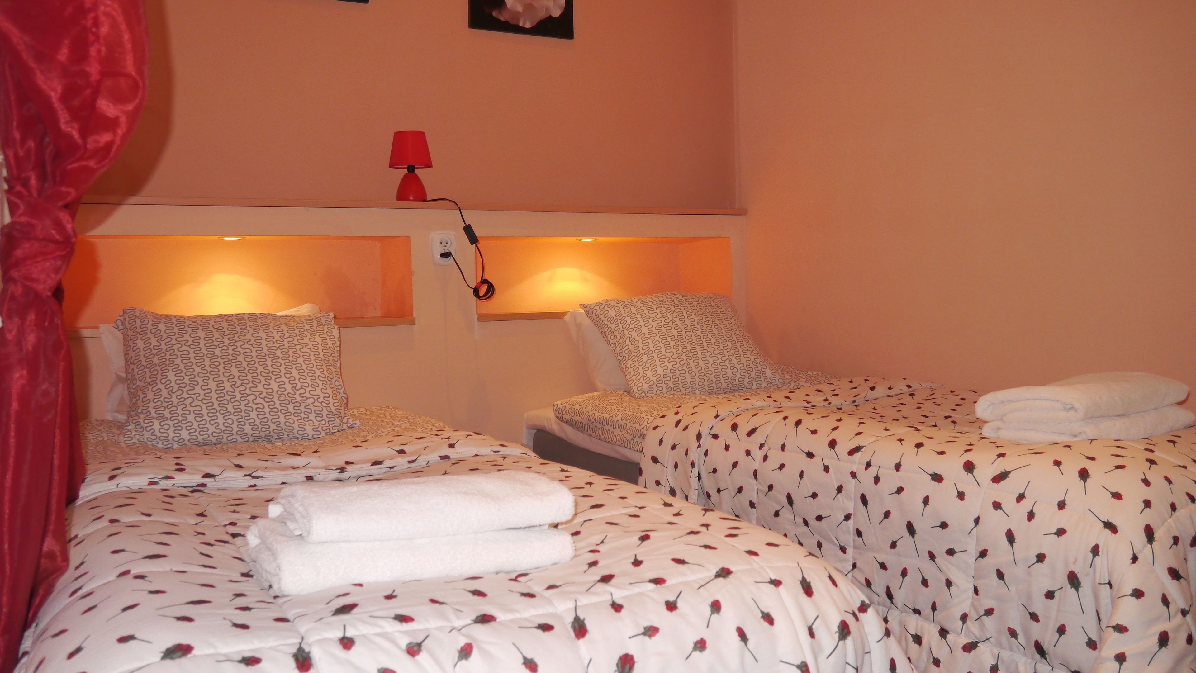 A hotel room with two beds, each with patterned bedding and pillows, a red lamp, and a wall-mounted phone.