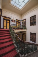 A grand staircase with red carpeted steps leading to a balcony with plants.