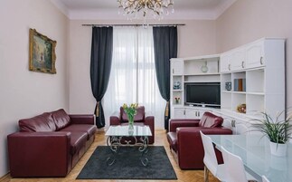 A living room with two red leather sofas, a glass coffee table, a TV on a white stand, and a white shelving unit with decorative items.