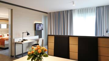 Habitación de hotel con cama, escritorio, televisión y ventana con cortinas.