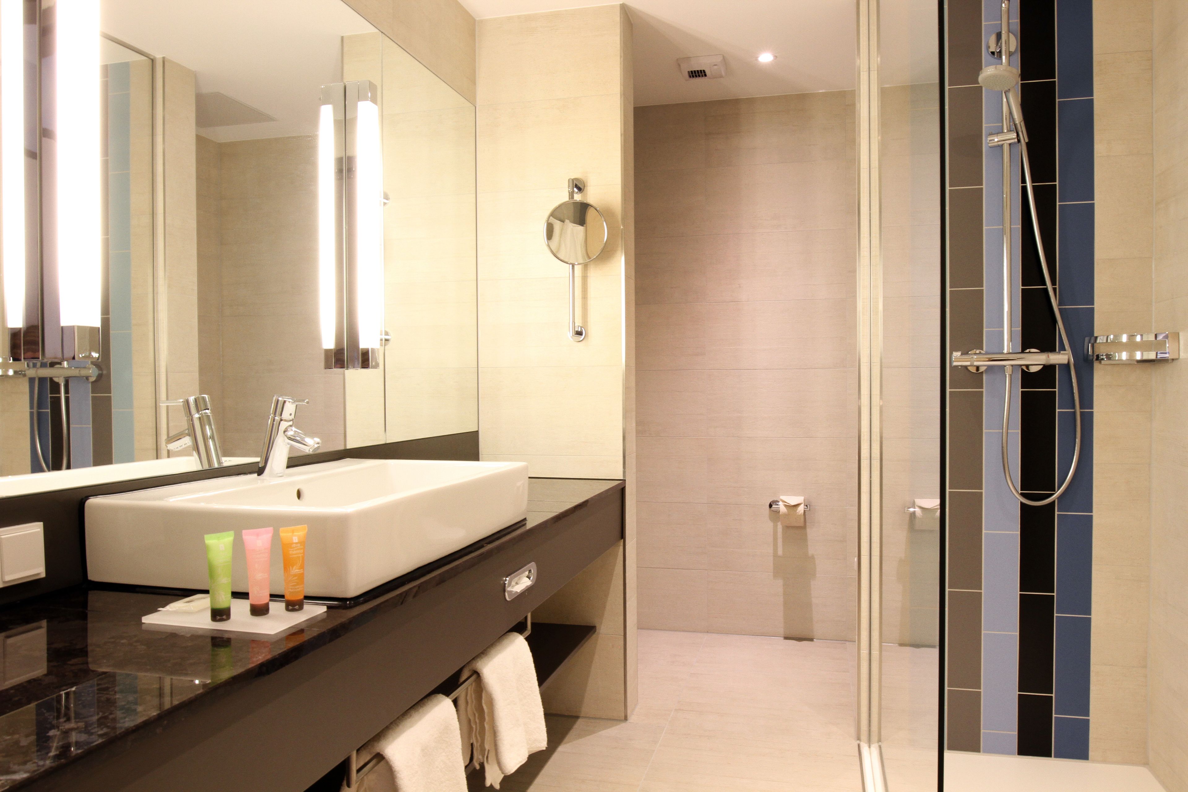 A modern bathroom with a large mirror, a sink, and a shower area.
