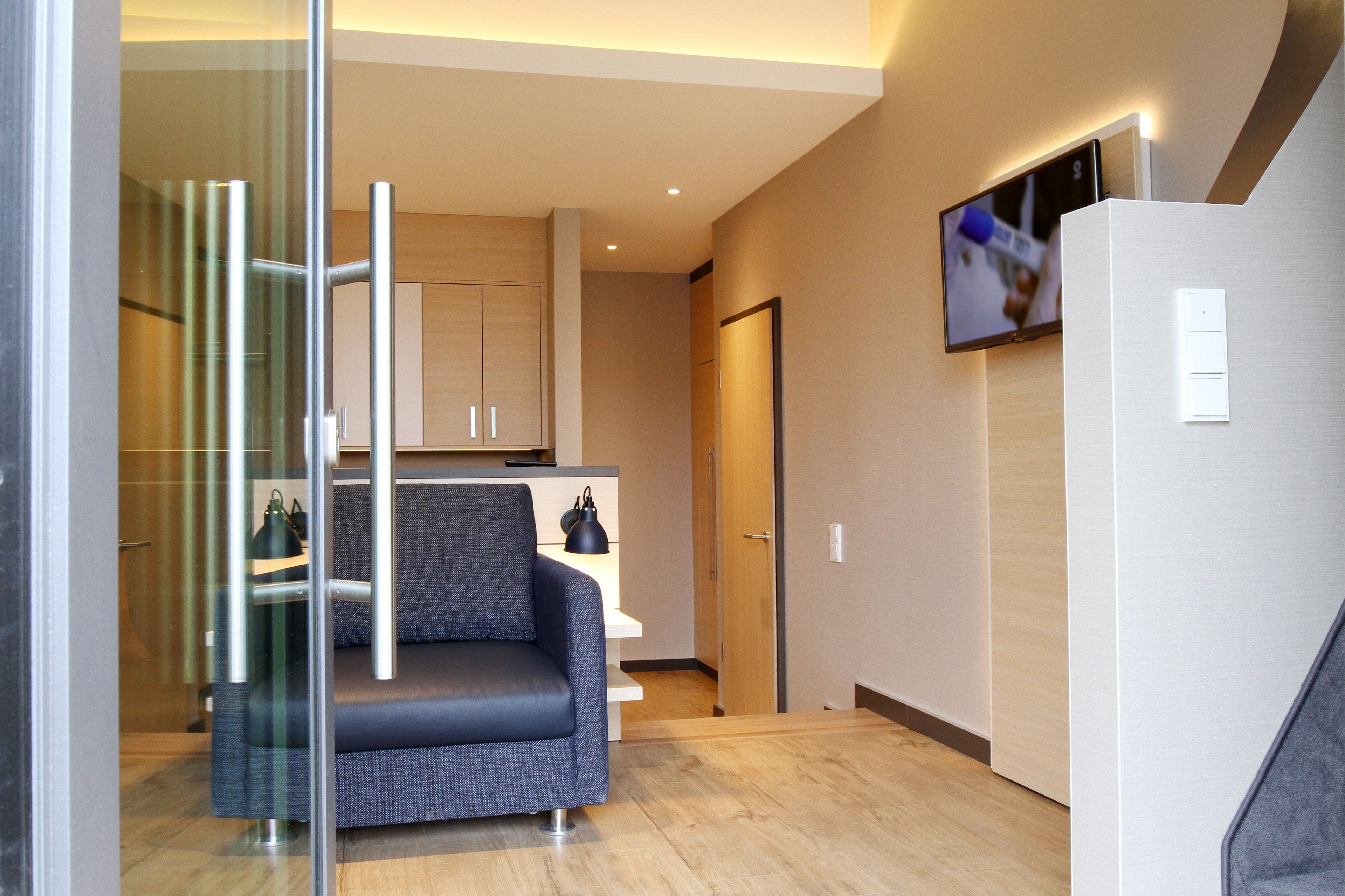 A modern hotel room with a sofa, a TV mounted on the wall, and a wooden floor.
