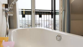 A modern bathroom with a large bathtub, a showerhead, and a view of a snowy landscape through a window.
