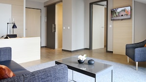 A modern living room with a sofa, a coffee table with decorative items, a flat-screen TV mounted on the wall, and a door leading to another room. - Hafenhotel Meereszeiten (Heiligenhafen)