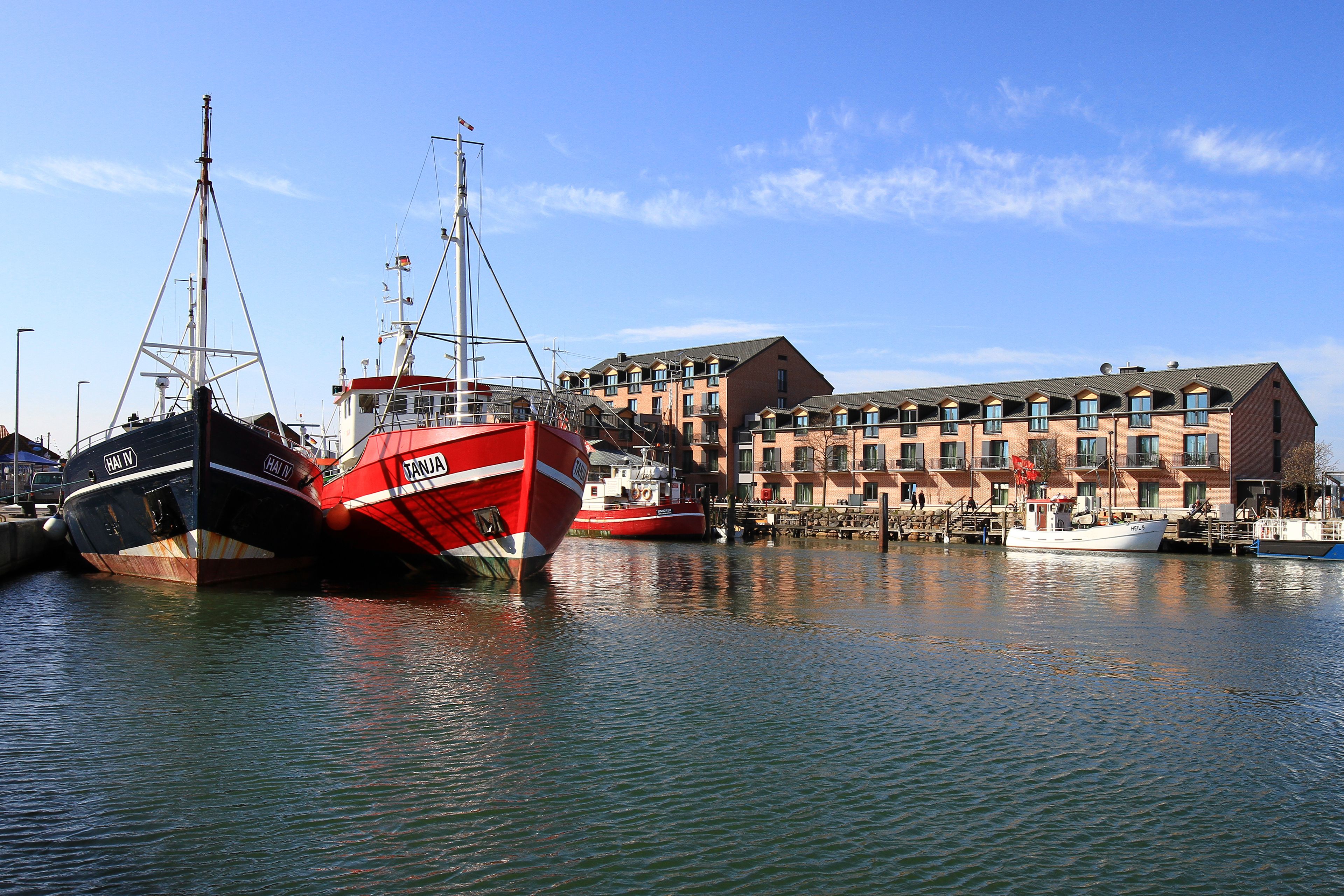 A marina with several boats docked, a building with multiple windows and balconies, and a clear sky.