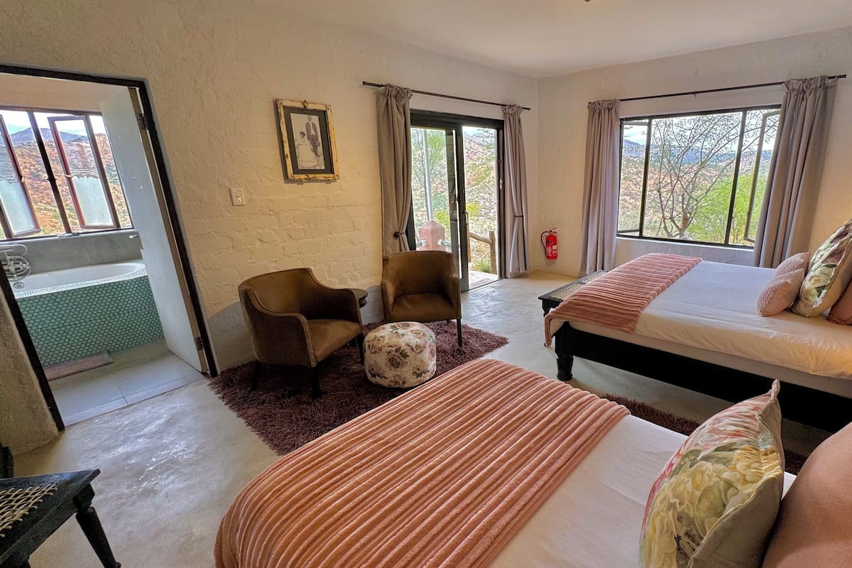 A bedroom with a bed, two chairs, a small table, and a window with curtains.