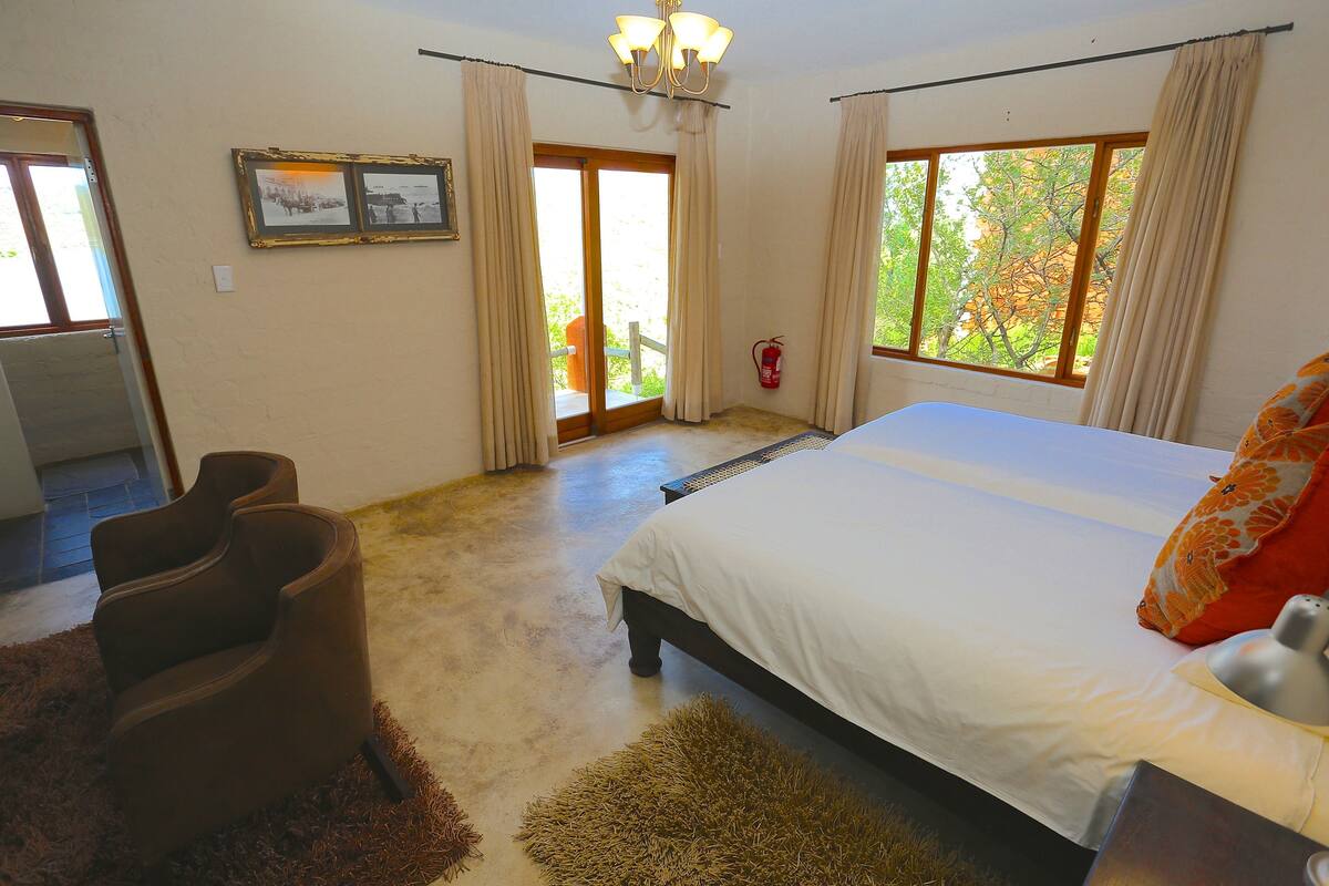 A bedroom with a bed, a chair, a fire extinguisher, and a window with a view.