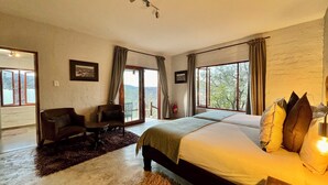 A spacious bedroom with a large bed, a desk, and a chair, featuring large windows and a view of the outdoors. - River Crossing Lodge (Windhoek)