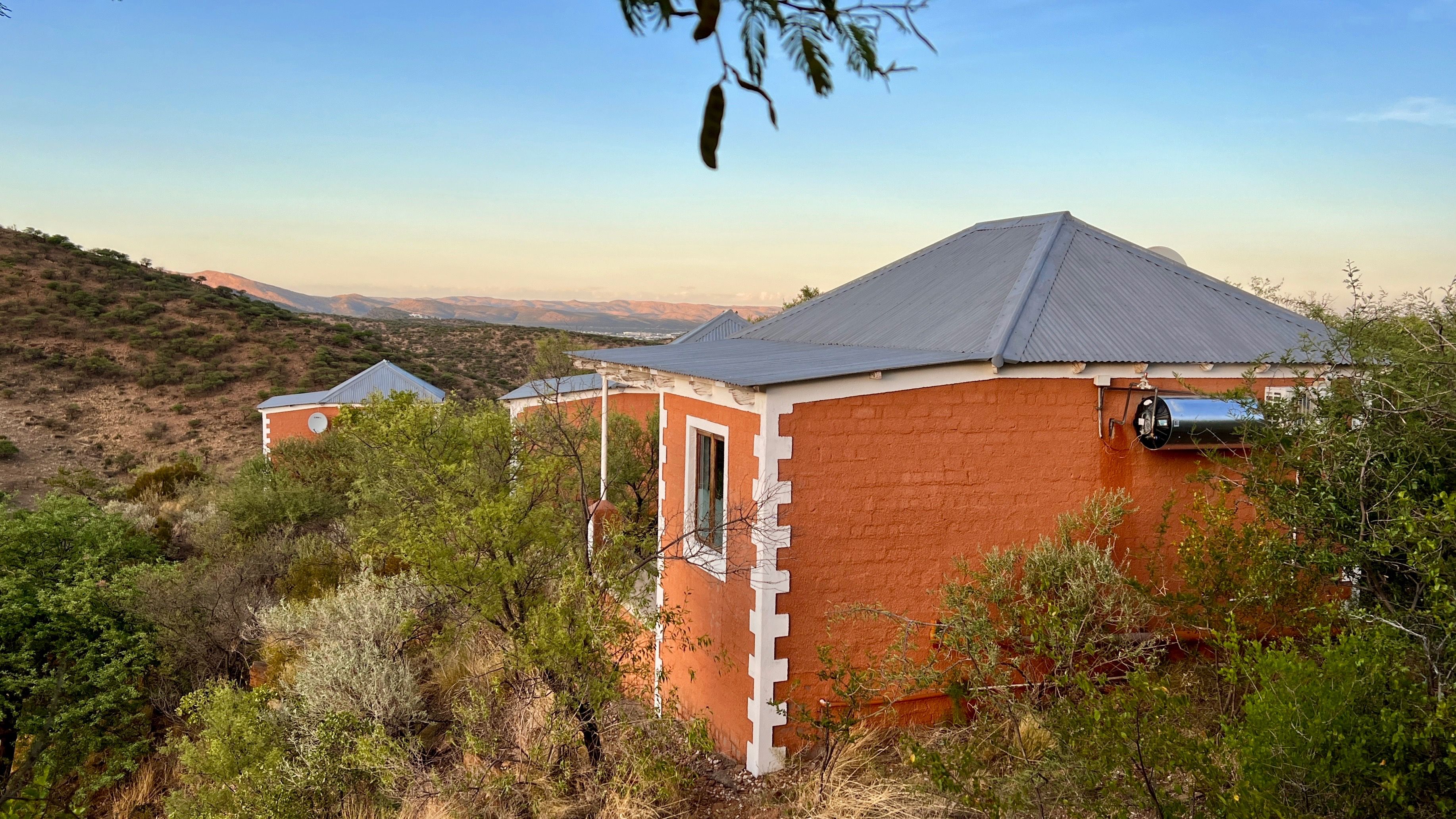 A building with a sloped roof, surrounded by dense vegetation and hills in the background.