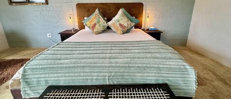A neatly made bed with a striped blanket, two floral pillows, and two bedside lamps.