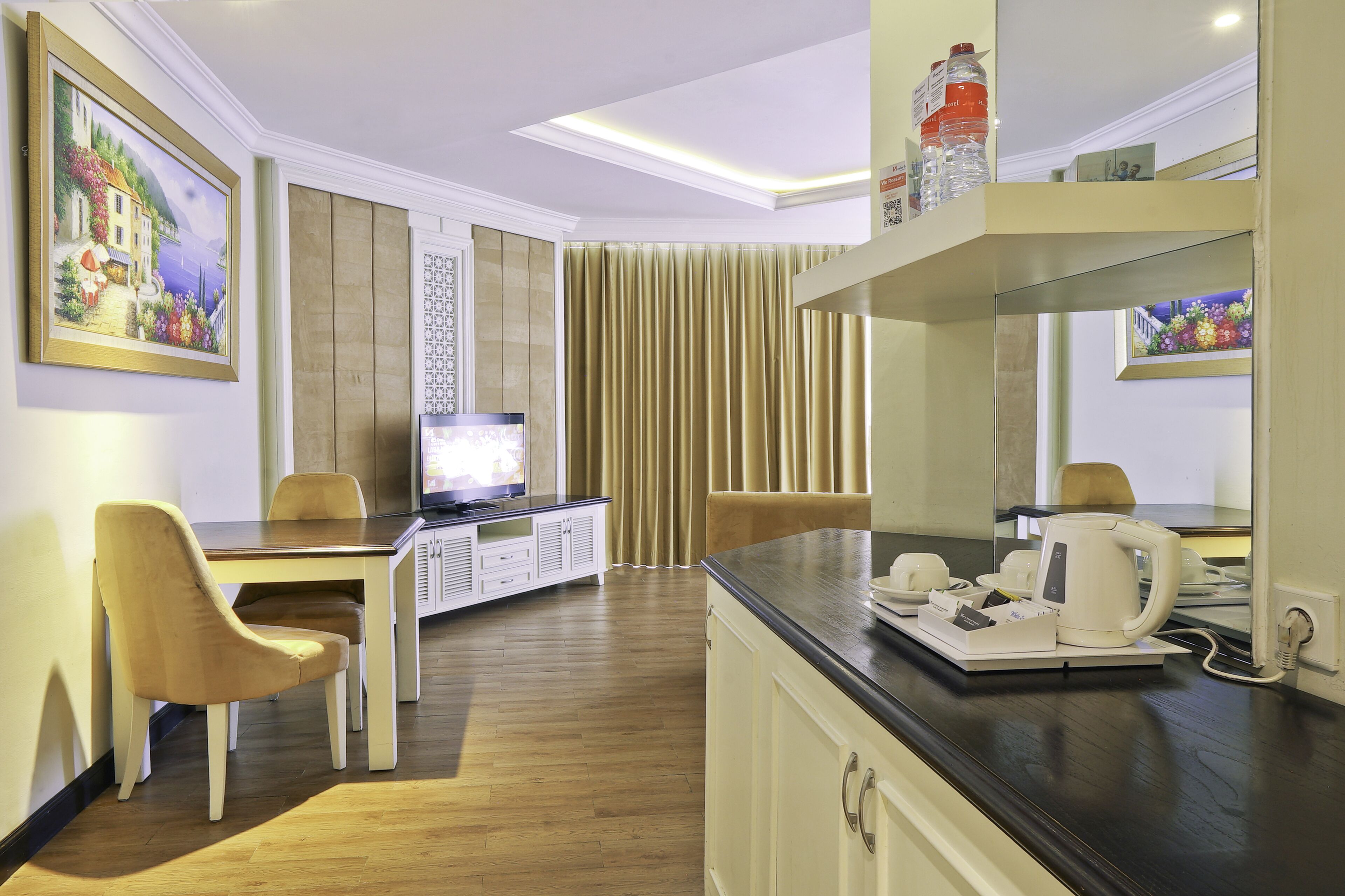 A modern hotel room with a dining area, a television, a coffee maker, and a minibar.