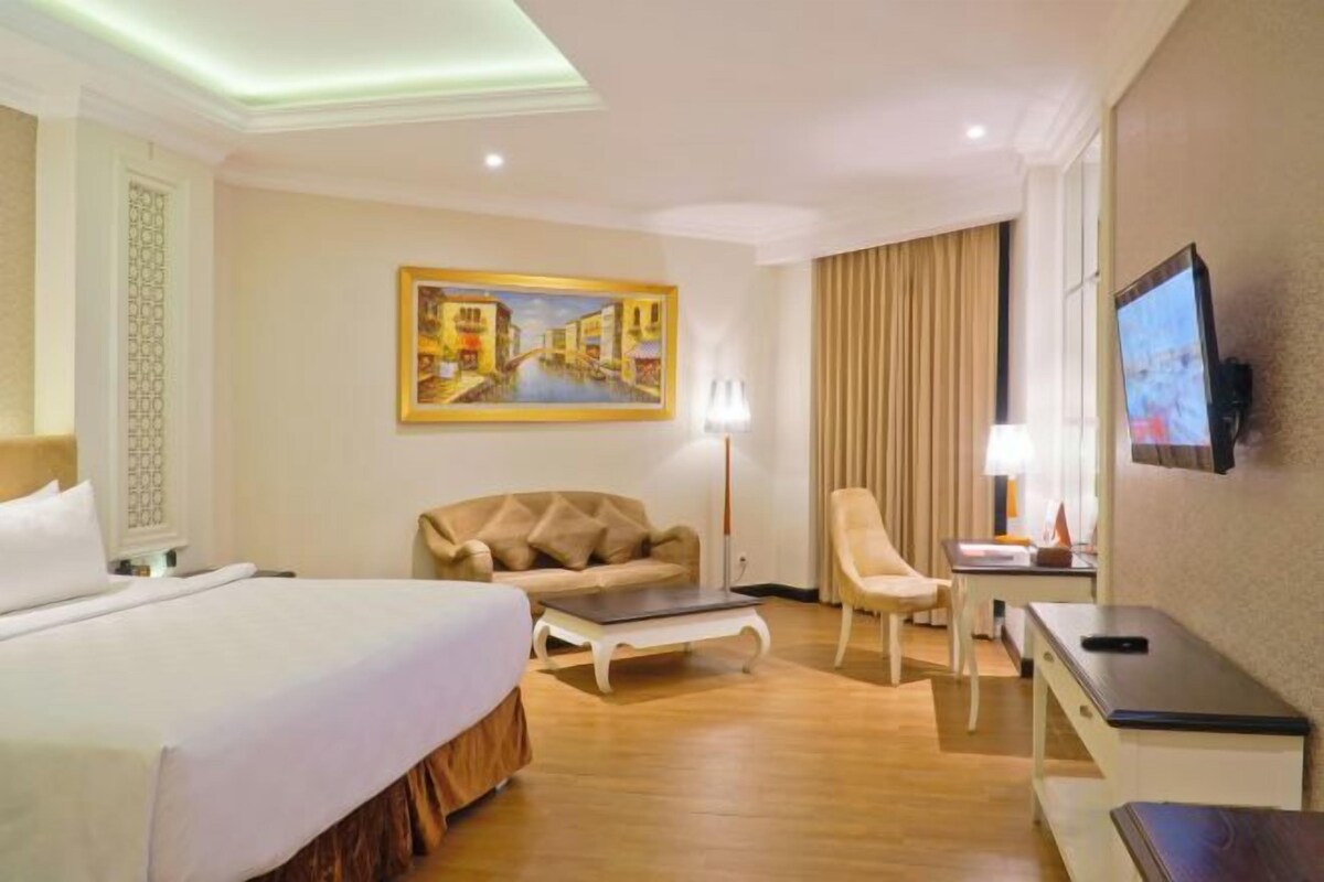 Habitación de hotel con cama, sofá, escritorio, silla, televisor y un cuadro en la pared.