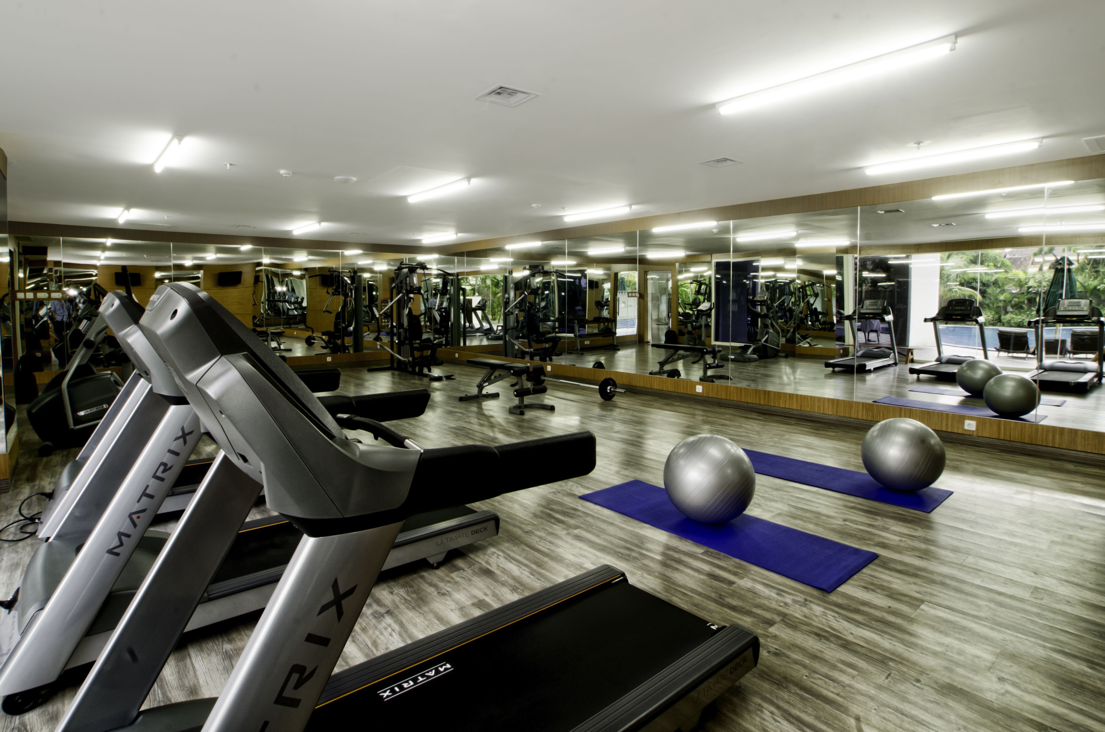 Ein Fitnessraum mit Laufbändern, Übungsbällen und einer Spiegelwand.