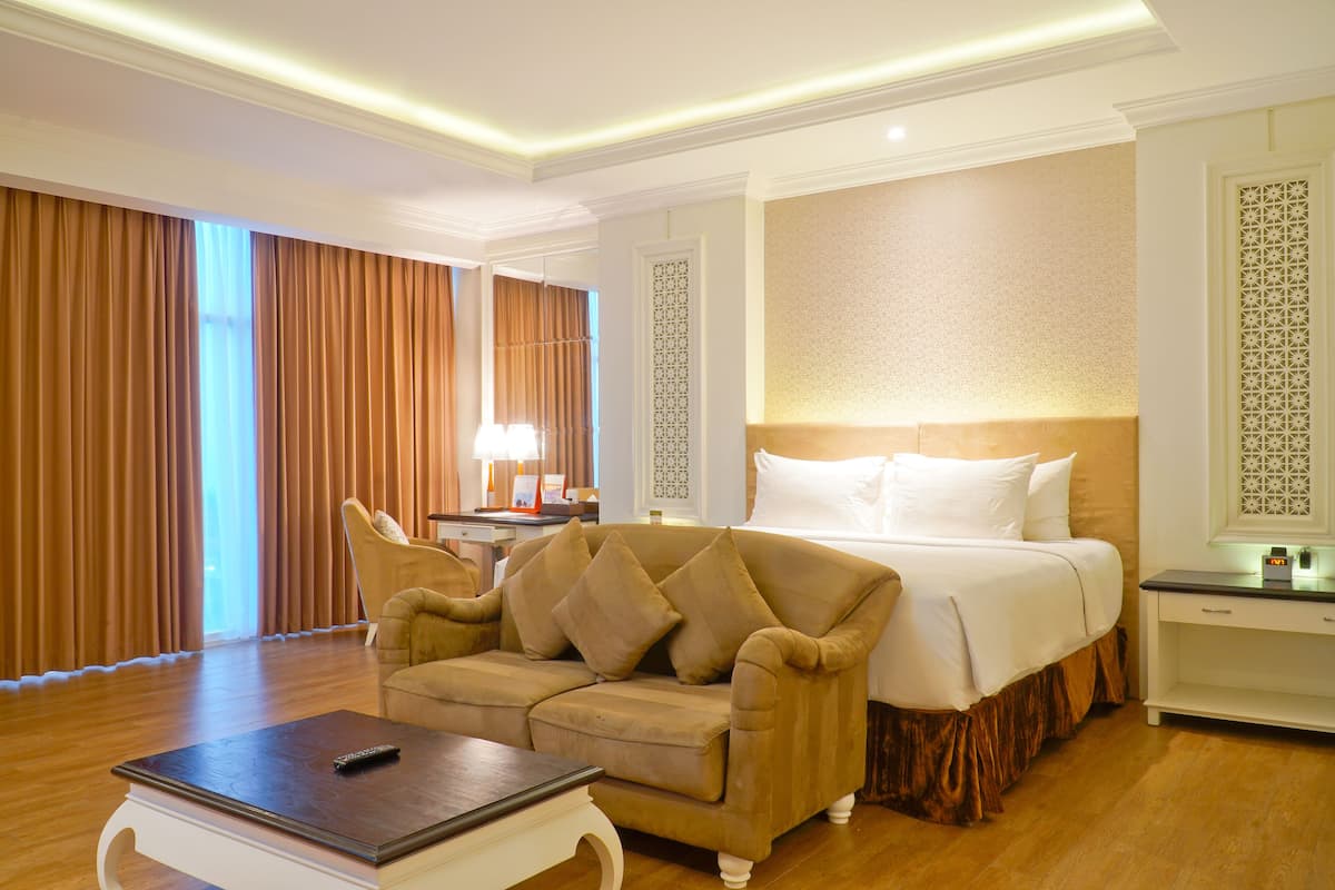Une chambre d’hôtel avec un grand lit, un canapé, une table de chevet et une lampe.