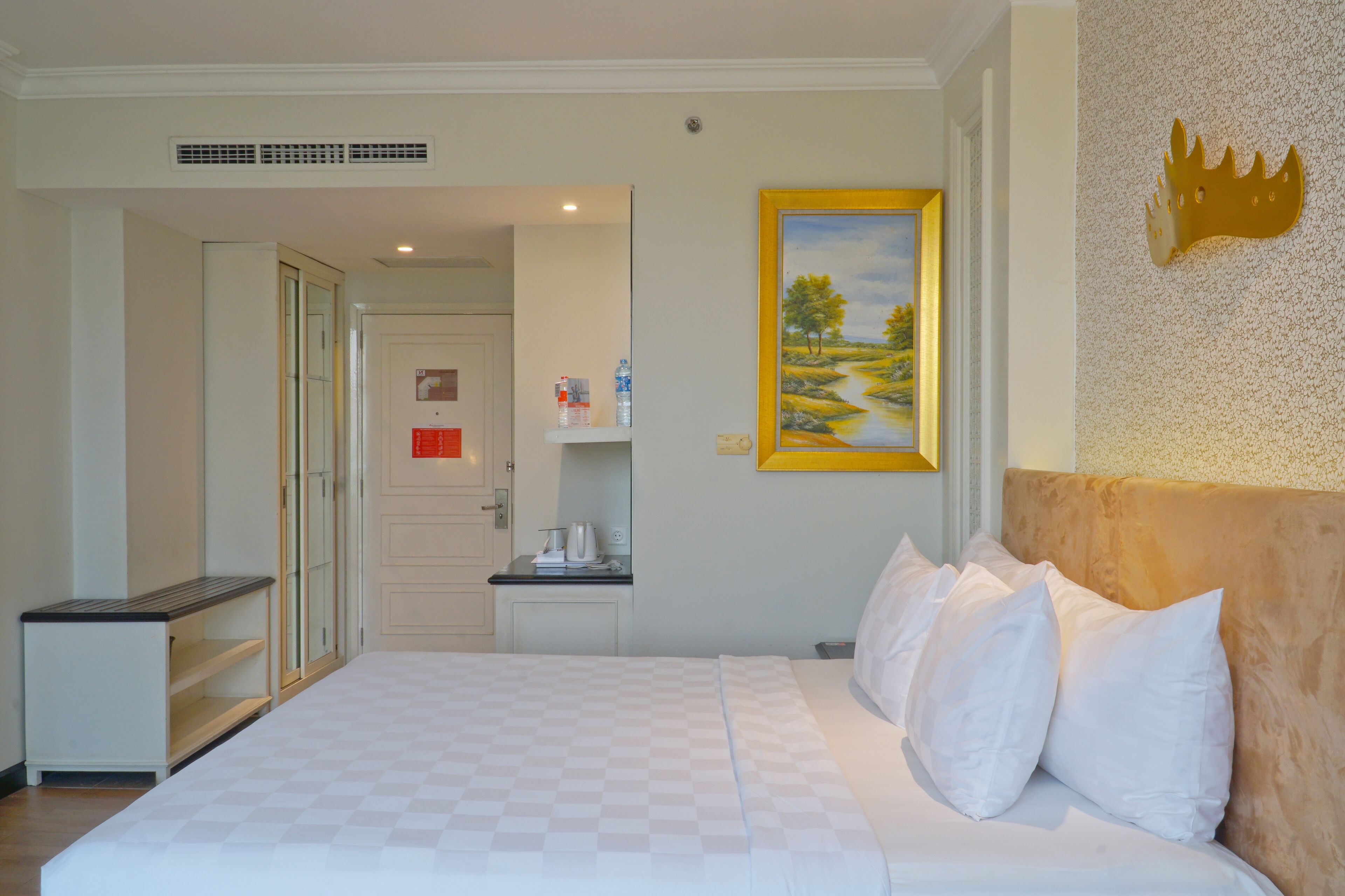 Ein Hotelzimmer mit einem großen Bett, einem Nachttisch mit Wasserkocher, einem kleinen Schreibtisch und einem gerahmten Bild an der Wand.