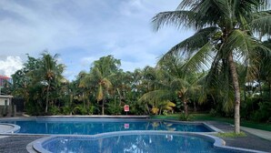 Une piscine dont le bord est revêtu de carrelage, entourée de palmiers et de verdure.