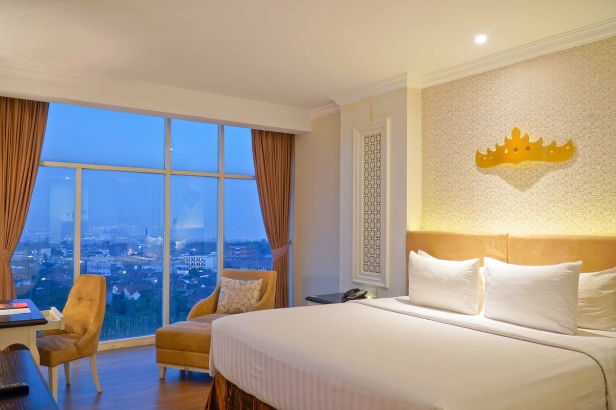 Une chambre d’hôtel avec une grande fenêtre, un lit, une chaise et un élément décoratif mural.