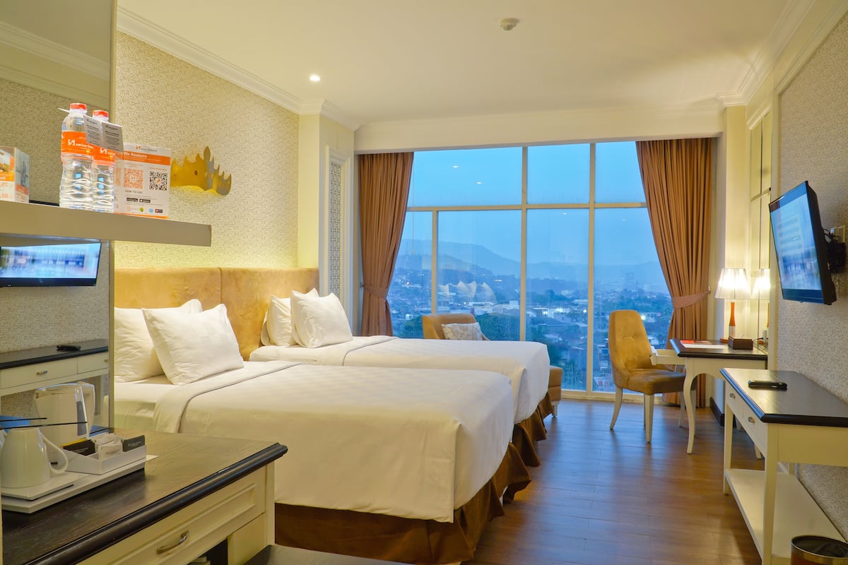 Une chambre d’hôtel avec deux lits, un bureau, une chaise, une télévision et une grande fenêtre donnant sur la ville.