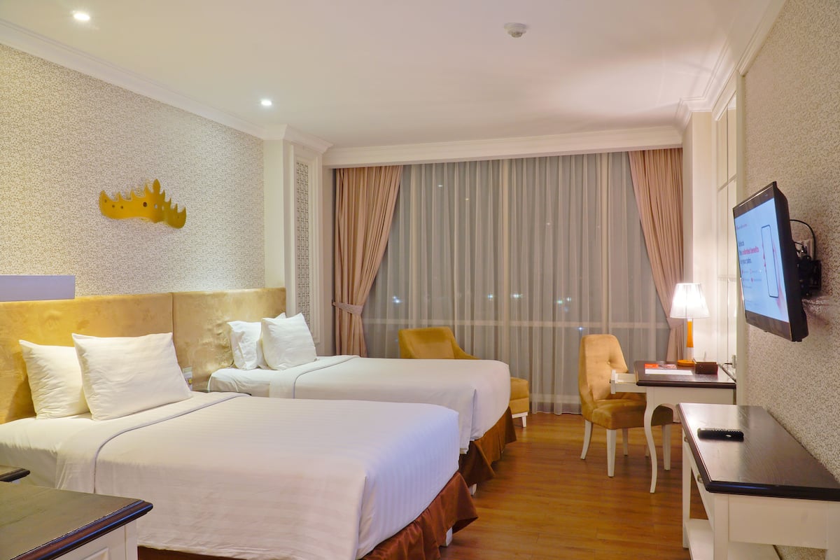 Une chambre d’hôtel avec deux lits, un bureau, une télévision et une fenêtre avec des rideaux.