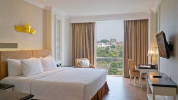 A hotel room with a large bed, a desk, a chair, a TV, and a balcony with curtains.