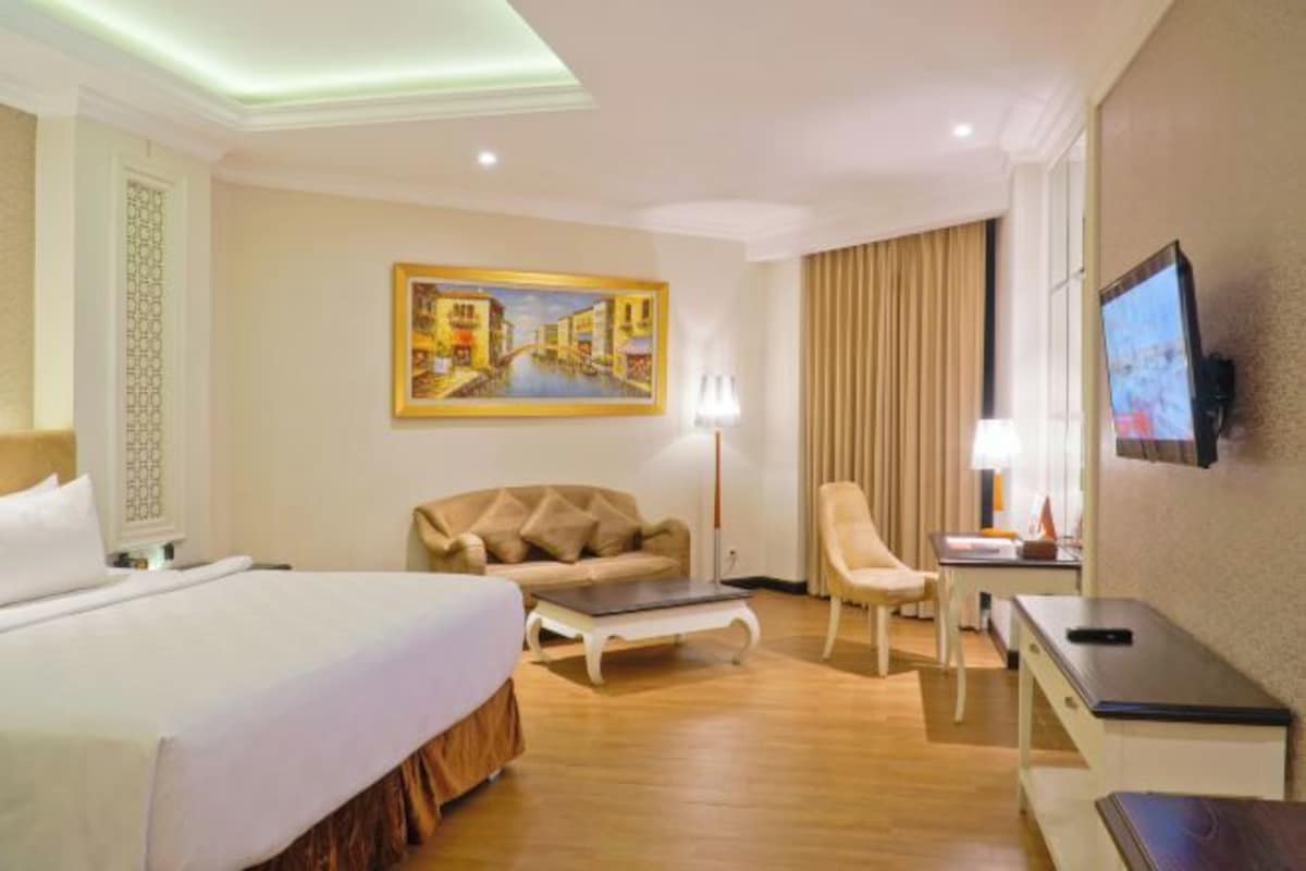 Une chambre d’hôtel avec un lit, un canapé, un bureau, une chaise, une télévision et un tableau au mur.