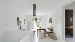 A spacious room with a high ceiling, a wooden dining table, a sofa, and a hanging light fixture. - Amalgam Homes Paros (Paros)