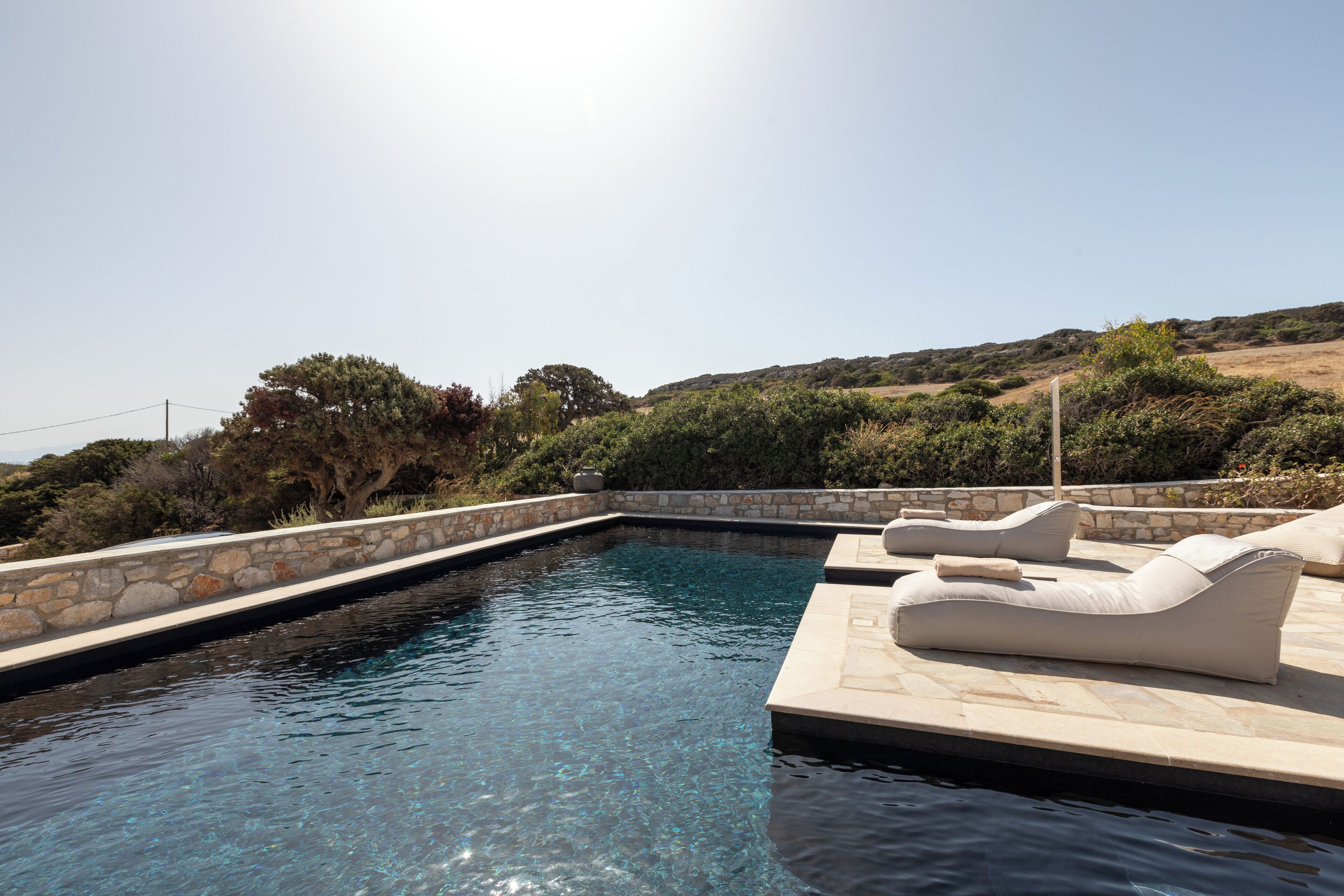 A swimming pool with lounge chairs and a stone wall.