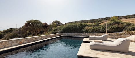 A swimming pool with lounge chairs and a stone wall.