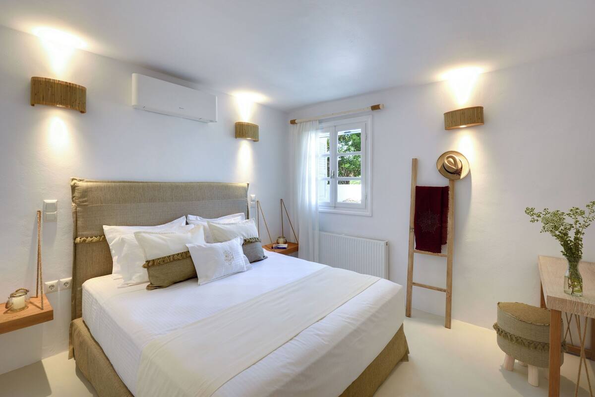 A neatly arranged bedroom with a large bed, bedside tables, a window with curtains, and a small table with a vase.