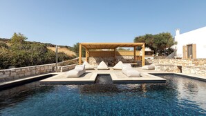 A clear blue pool with lounge chairs and a pergola, surrounded by stone walls and vegetation. - Amalgam Homes Paros (Paros)