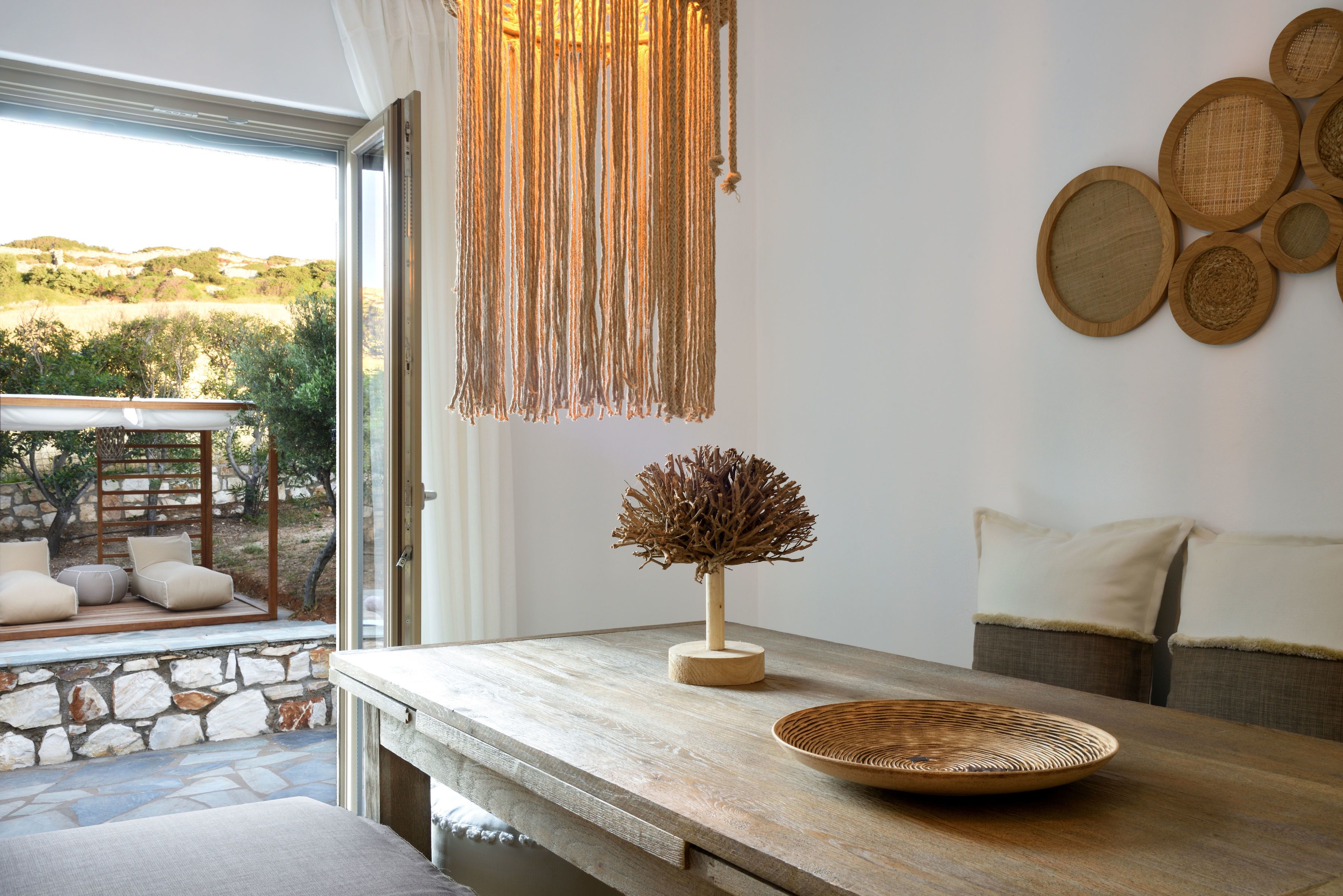 A wooden table with a woven bowl, a macramé light fixture, and a decorative tree sculpture.