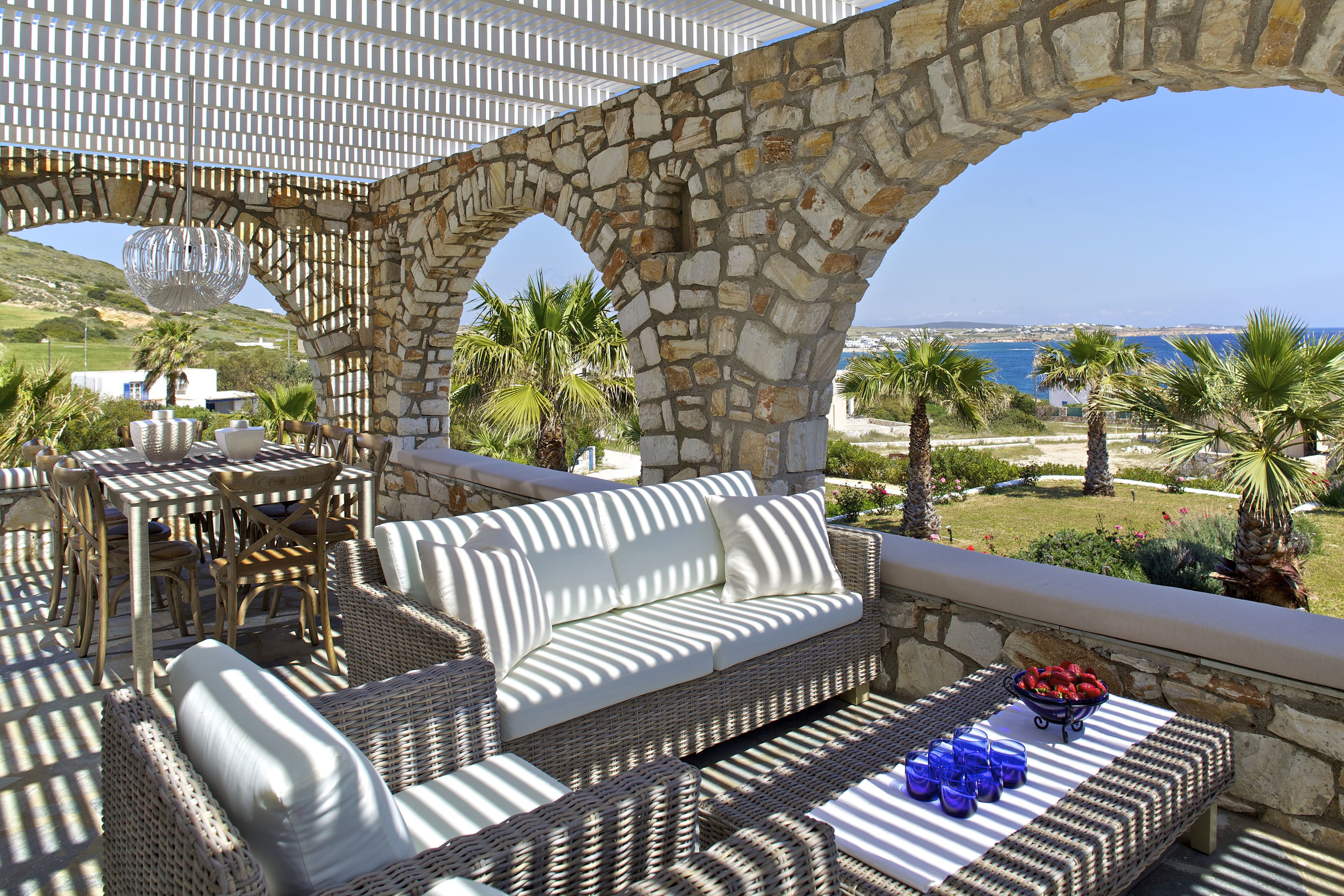 A stone archway leading to an outdoor seating area with wicker furniture and a view of the sea.