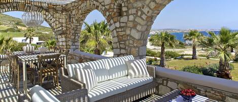 A stone archway leading to an outdoor seating area with wicker furniture and a view of the sea.