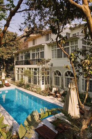 A two-story building with a swimming pool, surrounded by lush greenery and a large tree. - Villa Belle Epoque (Cairo)