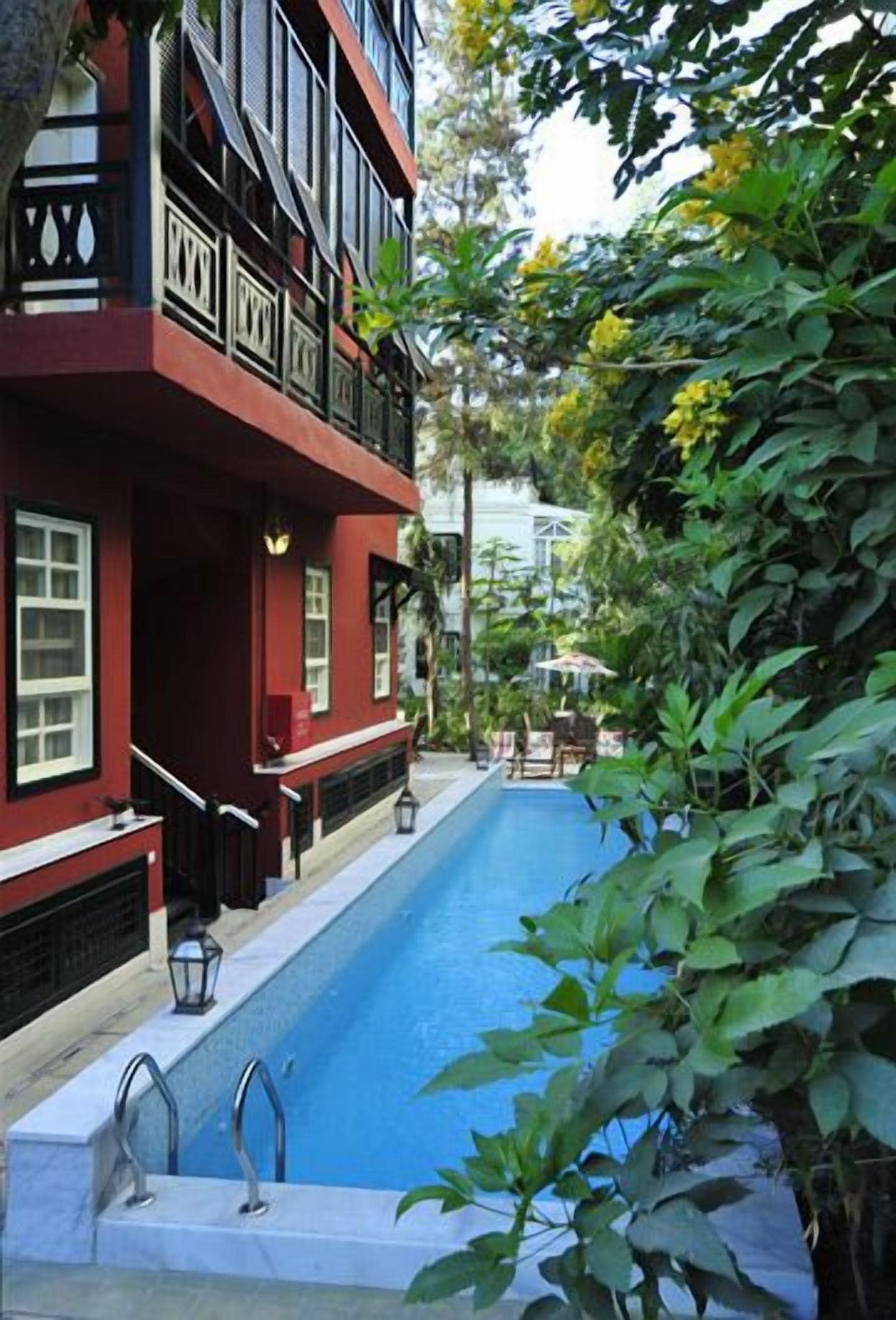 A swimming pool adjacent to a building with balconies and a garden area.