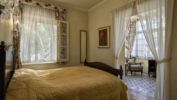 A bedroom with a large bed, a wooden dresser, a chair, and a window with sheer curtains.