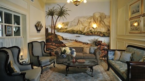 A living room with a mural of a coastal scene, two sofas, a coffee table, and a chandelier. - Villa Belle Epoque (Cairo)