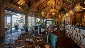 Een ruim restaurant met houten plafond, hangende rieten lampen en diverse zithoeken.