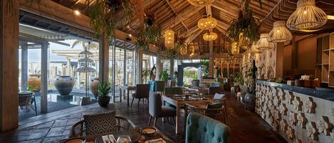 A spacious restaurant with wooden ceiling, hanging wicker lamps, and a variety of seating arrangements.