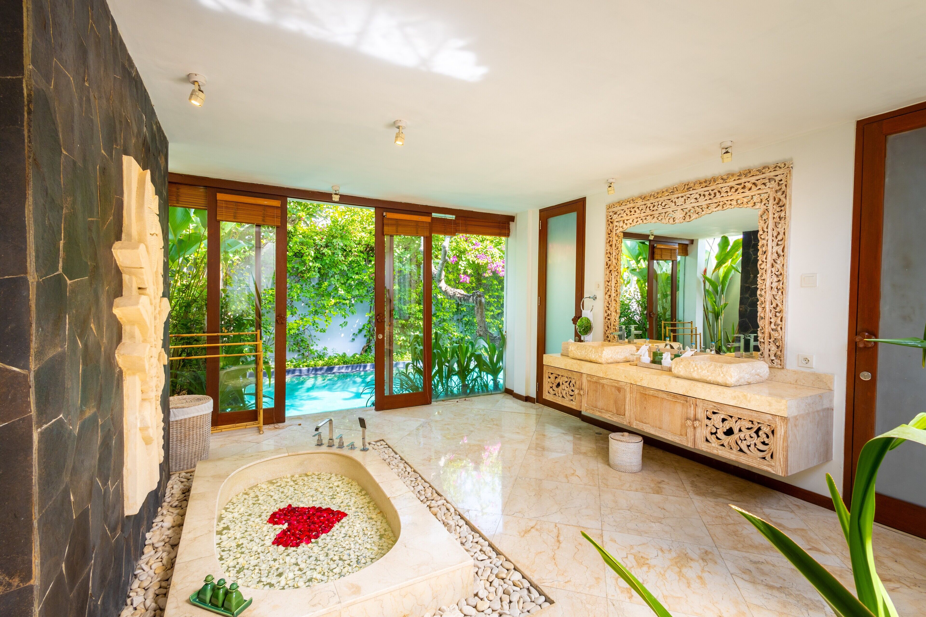 Un baño moderno con una bañera grande, un tocador con espejo y vistas a una piscina y zonas verdes.