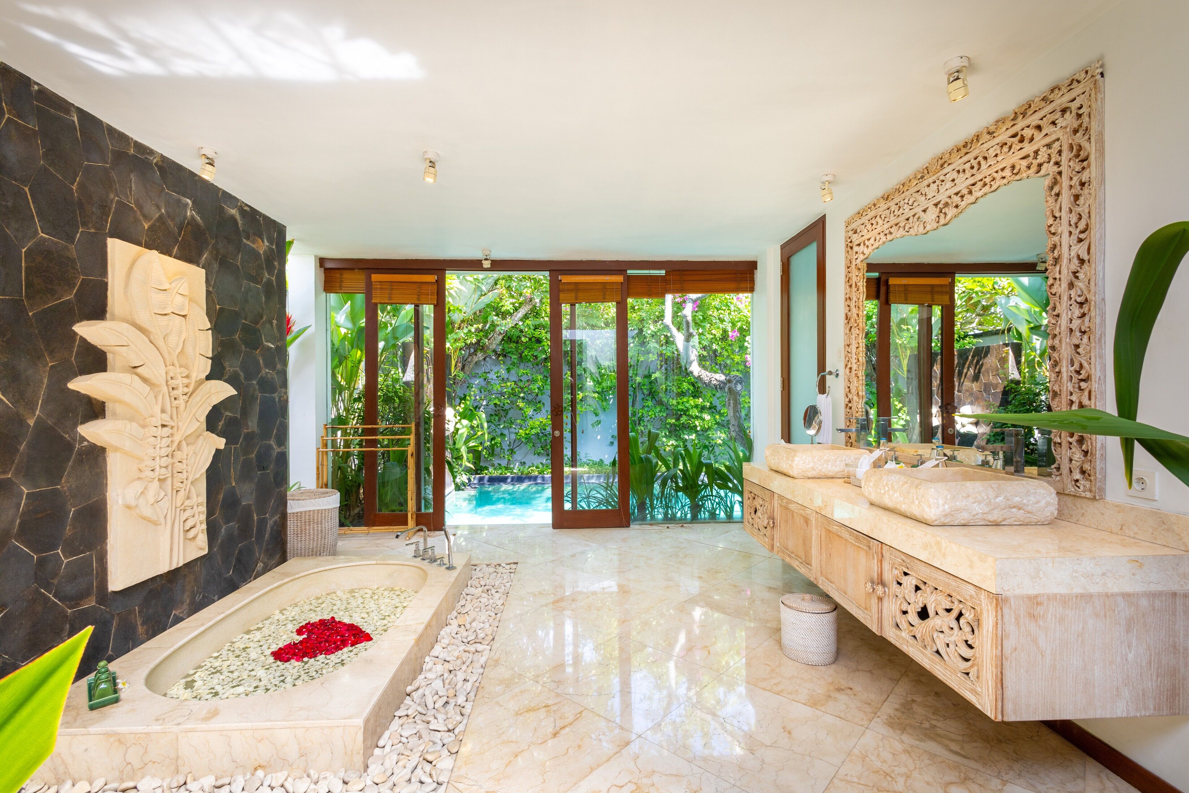 A luxurious bathroom with a marble floor, a large bathtub, a stone wall with a carved design, and a large mirror.