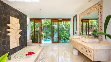 A luxurious bathroom with a marble floor, a large bathtub, a stone wall with a carved design, and a large mirror.