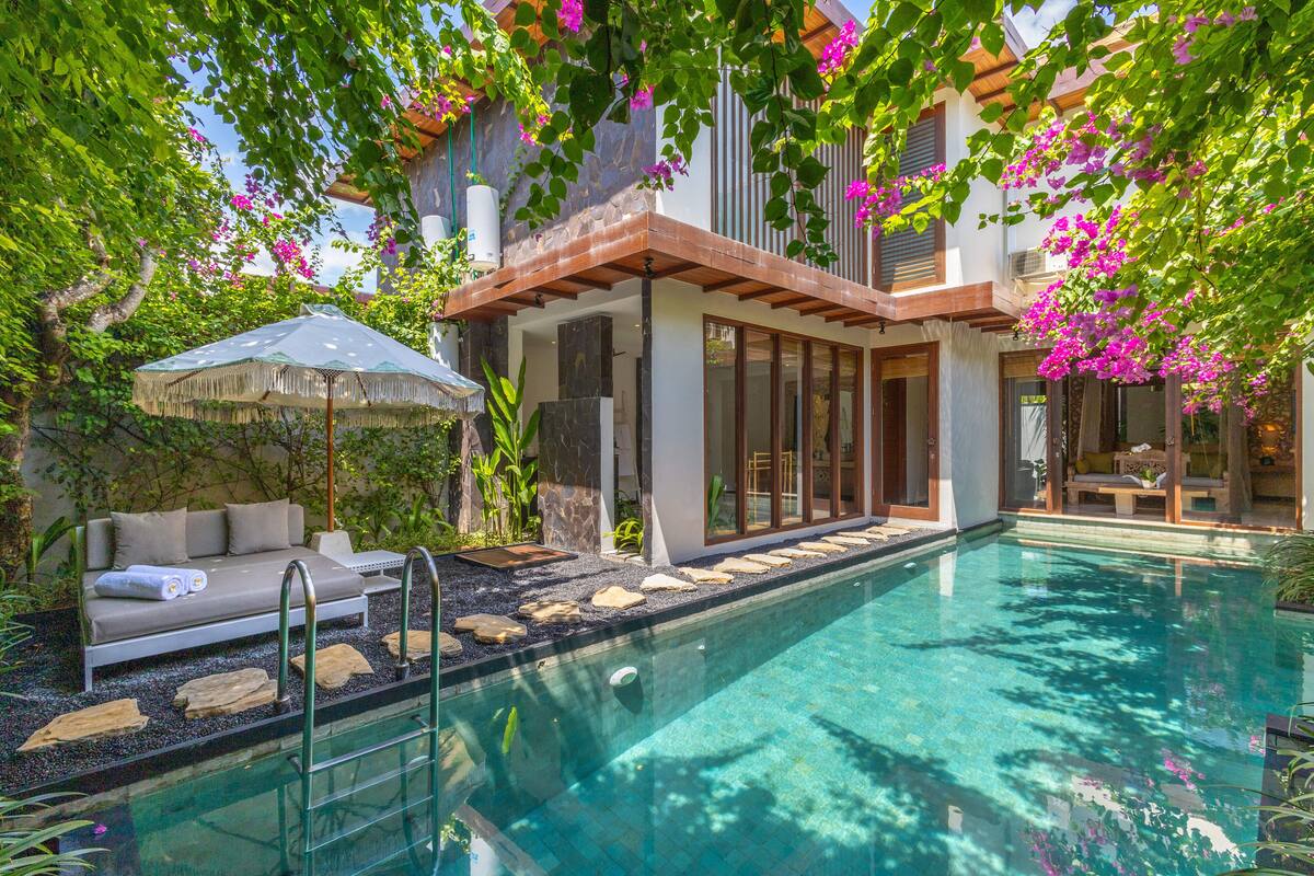 A modern outdoor pool area with a stone-lined edge, a lounge with a canopy, and a stone wall.