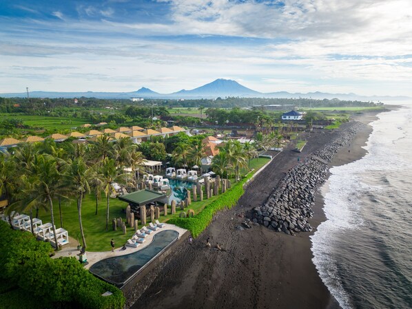 An aerial view of a coastal resort with a swimming pool, lounge chairs, and a rocky shoreline. - The Royal Purnama Beach Boutique Villas - Adult Only (Sukawati)