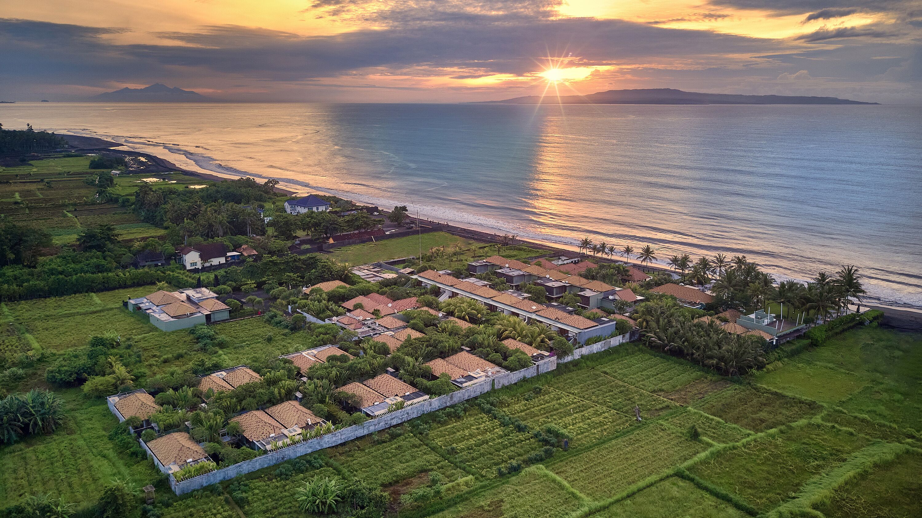 An aerial view of a coastal residential area with houses, a beach, and a sunset.