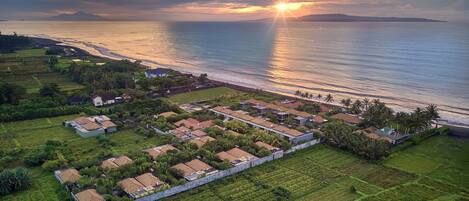 Vista aérea de una zona residencial costera con casas, una playa y un atardecer.